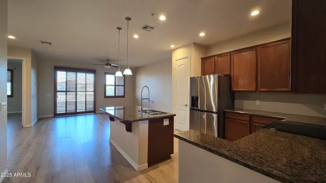 a kitchen with stainless steel appliances granite countertop a refrigerator a sink dishwasher and wooden cabinets with wooden floor