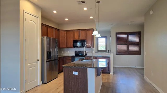 a kitchen with kitchen island granite countertop wooden cabinets a refrigerator a sink a stove and a wooden floors