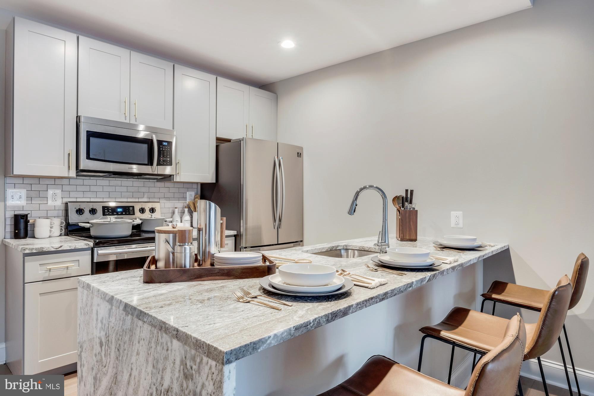 30 North 23rd Street, Unit 2402 Philadelphia, PA 19103 - Photo 5 of 42 a kitchen with stainless steel appliances kitchen island granite countertop a table chairs stove and refrigerator
