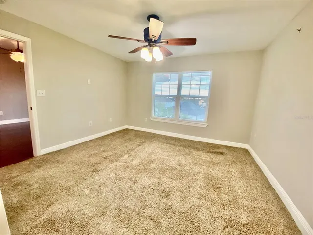 an empty room with chandelier fan and windows