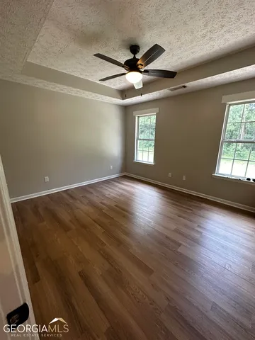 an empty room with wooden floor fan and windows