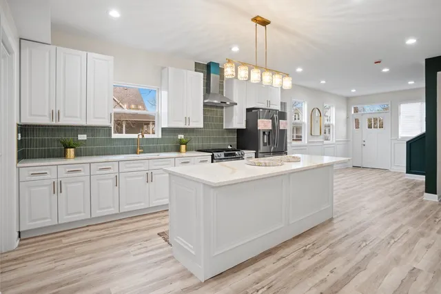 a kitchen with stainless steel appliances kitchen island granite countertop a sink a stove a refrigerator and white cabinets with wooden floor