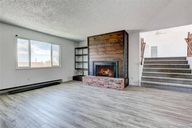 a view of an empty room with wooden floor fireplace and a window