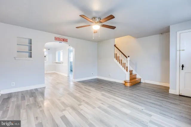 a view of an empty room with wooden floor and a ceiling fan