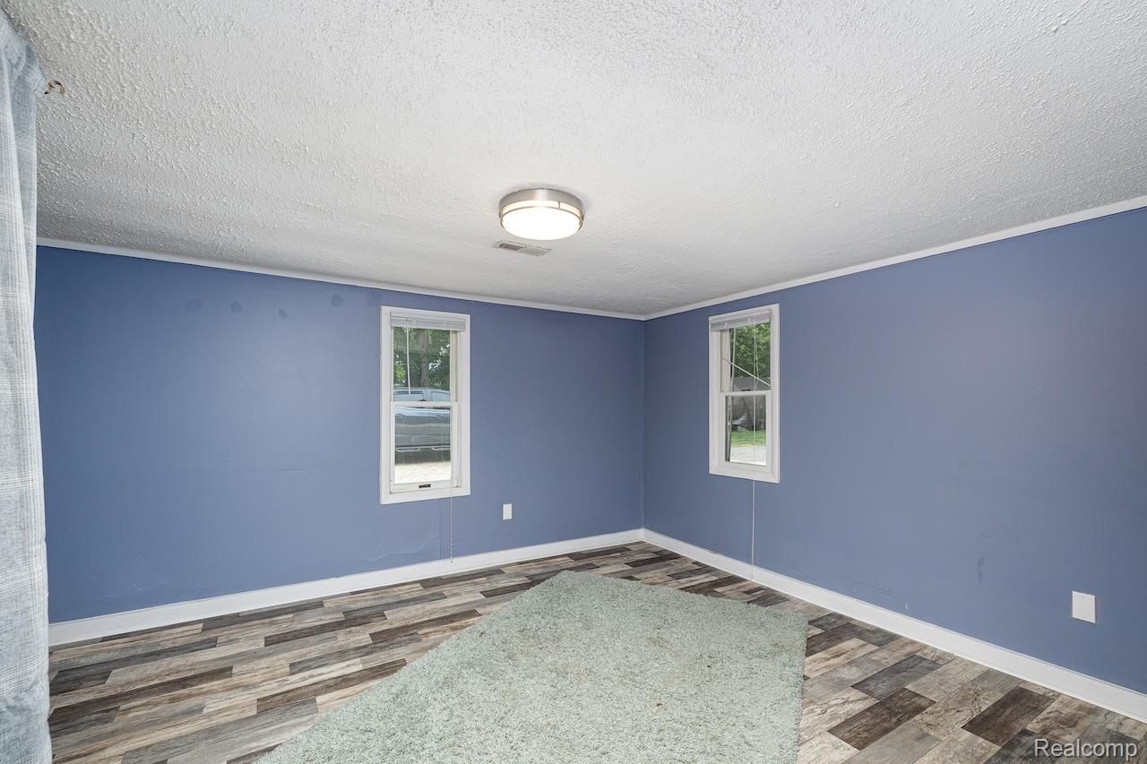 8595 Orchard Road Pinckney, MI 48169 - Photo 13 of 25 Spacious room featuring fresh periwinkle walls, recessed ceiling lighting, wood-finish flooring with mixed-tone planks, and dual casement windows with white trim allowing natural light throughout