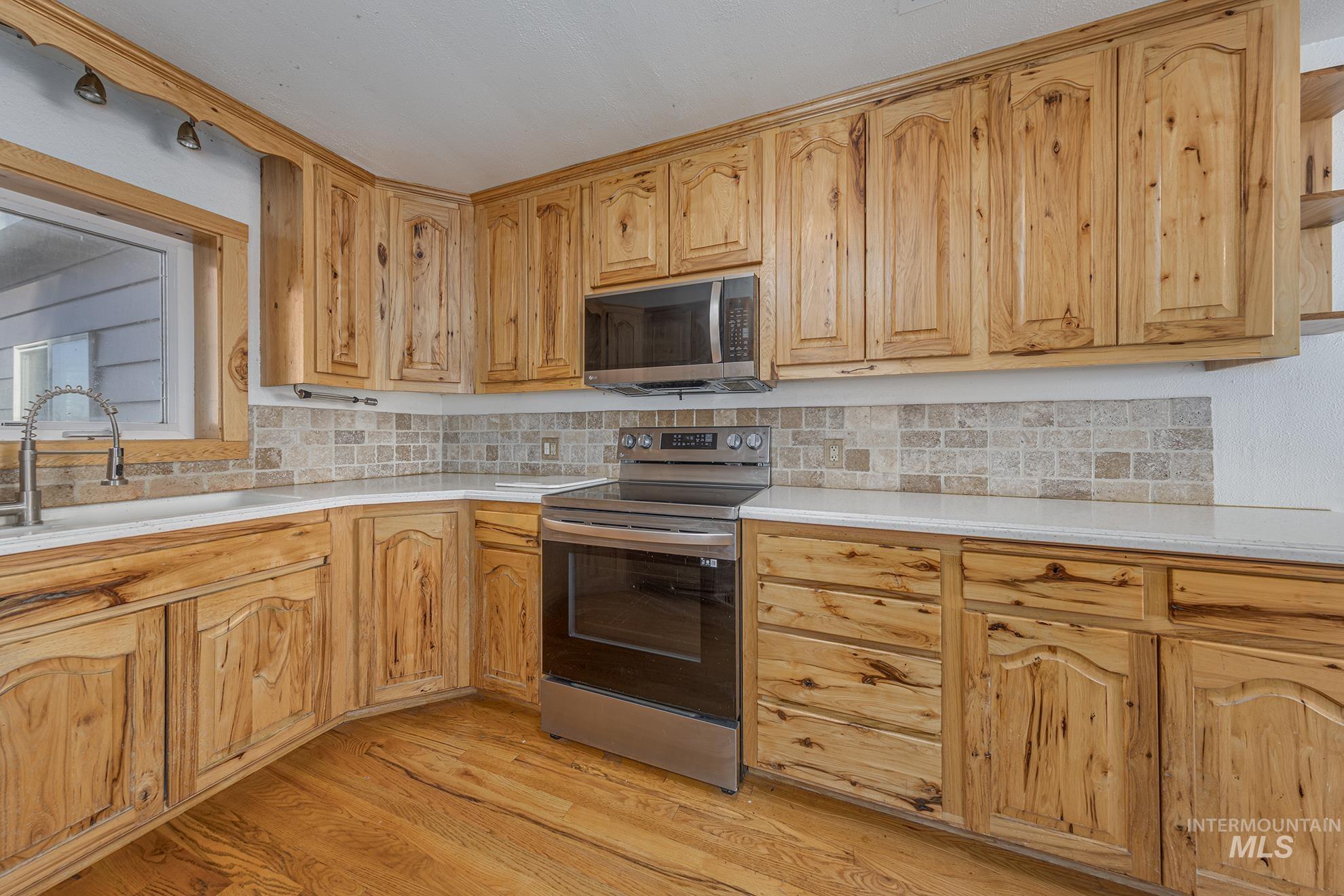 28552 Market Road Caldwell, ID 83607 - Photo 4 of 50 Kitchen with appliances with stainless steel finishes, light wood-style floors, decorative backsplash, and light stone countertops