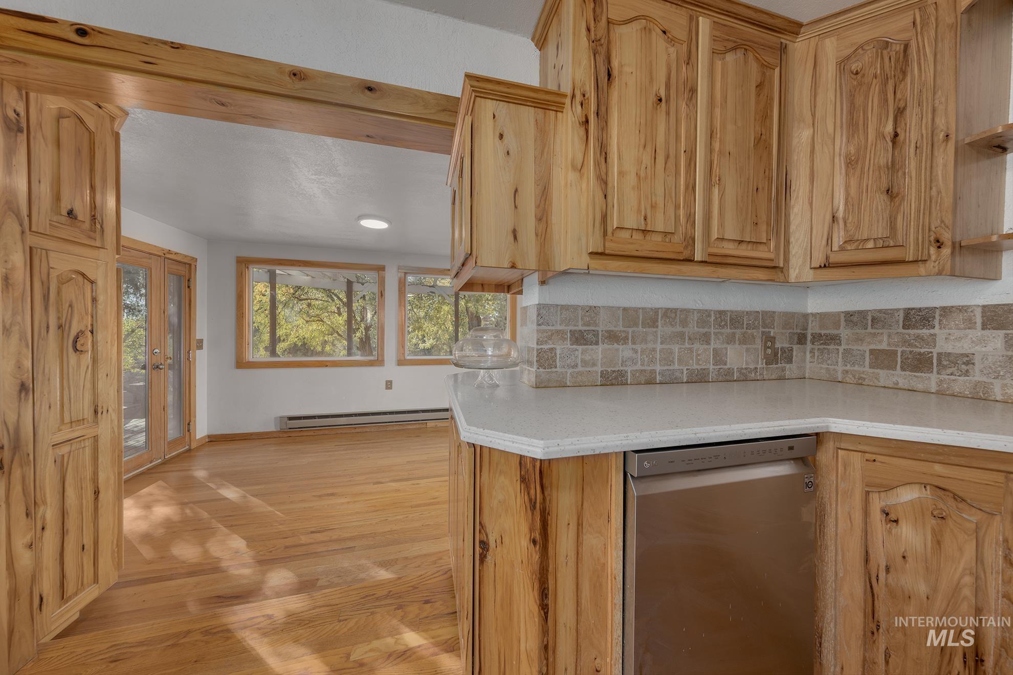 28552 Market Road Caldwell, ID 83607 - Photo 5 of 50 Kitchen with stainless steel dishwasher, light wood-style floors, backsplash, light brown cabinetry, and a baseboard radiator