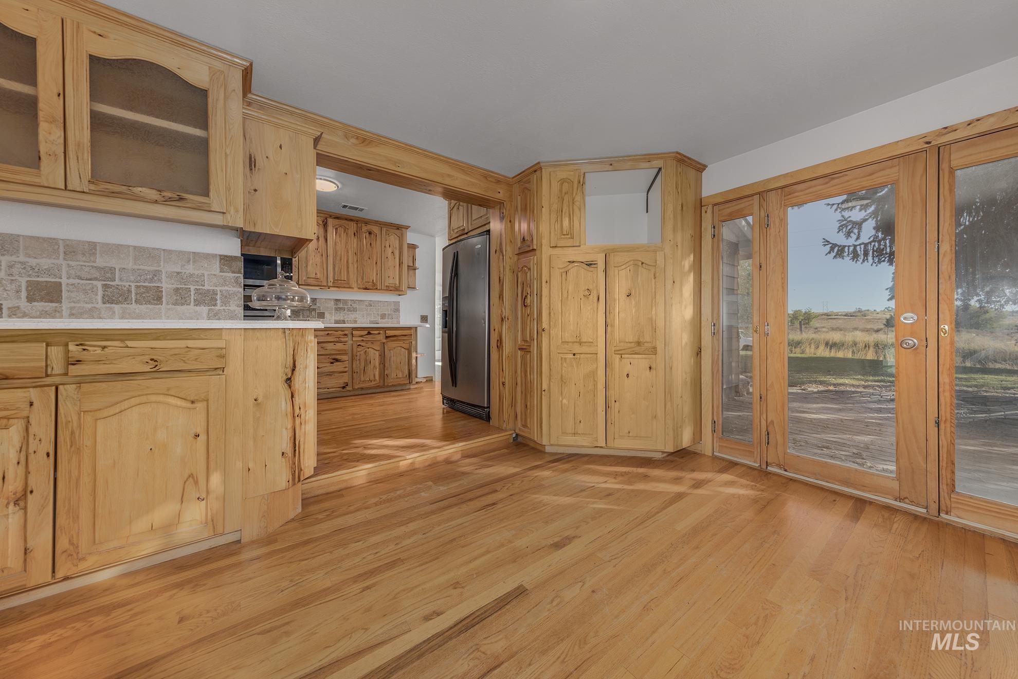 28552 Market Road Caldwell, ID 83607 - Photo 9 of 50 Kitchen with glass insert cabinets, light wood finished floors, backsplash, stainless steel refrigerator with ice dispenser, and light brown cabinets