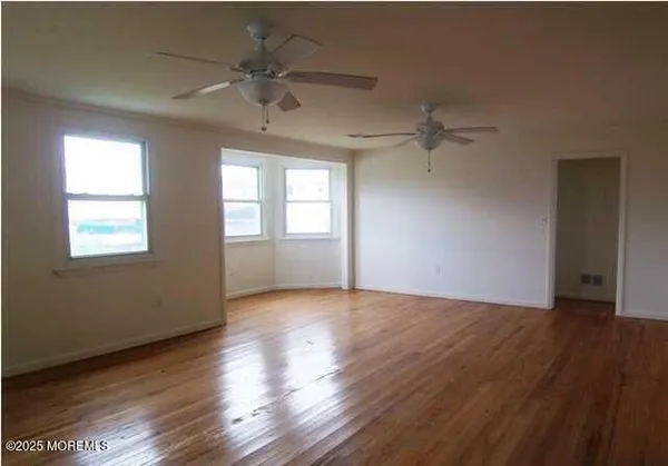 an empty room with wooden floor chandelier fan and windows