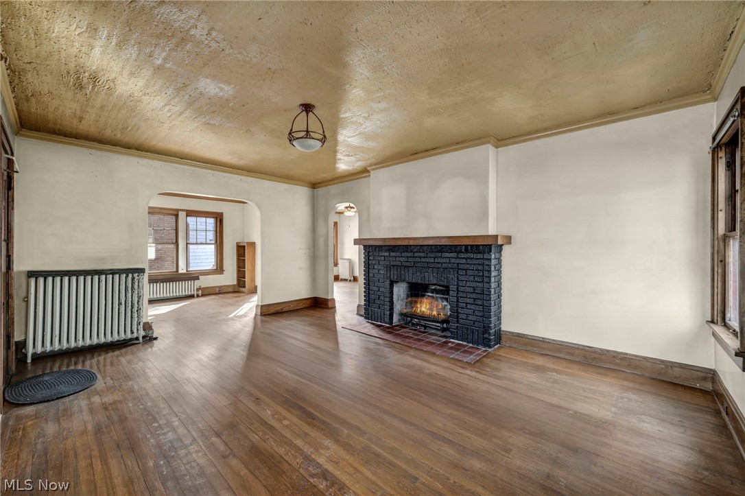 3272 Tullamore Road Cleveland, OH 44118 - Photo 5 of 47 Unfurnished living room with radiator, dark wood-style floors, a fireplace, arched walkways, and ornamental molding