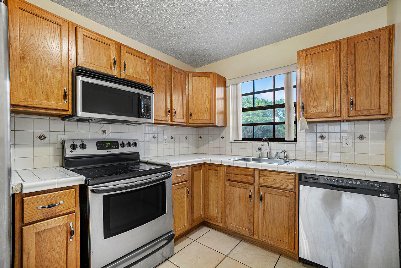 3050 Norwood Place, Unit N112 Boca Raton, FL 33431 - Photo 9 of 23 a kitchen with cabinets stainless steel appliances a sink and a microwave