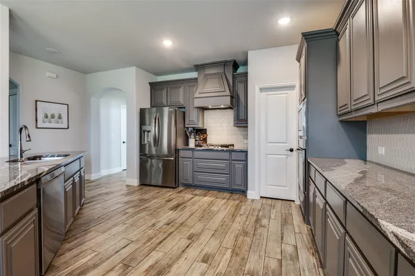 a kitchen with granite countertop a refrigerator oven a sink dishwasher and wooden cabinets with wooden floor