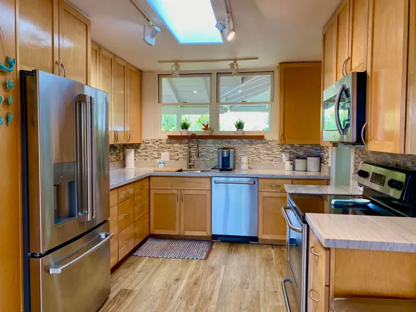 a kitchen with stainless steel appliances granite countertop a refrigerator a sink dishwasher a stove with wooden cabinets and floor