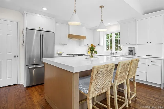 a kitchen with granite countertop a refrigerator a stove a sink and white cabinets with wooden floor