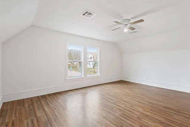 an empty room with wooden floor fan and windows