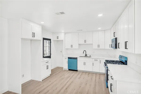 a kitchen with granite countertop a stove top oven a sink a refrigerator and white cabinets with wooden floor