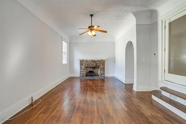 an empty room with wooden floor fireplace and windows