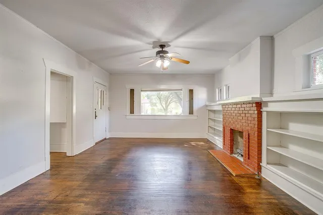 an empty room with wooden floor fireplace and windows