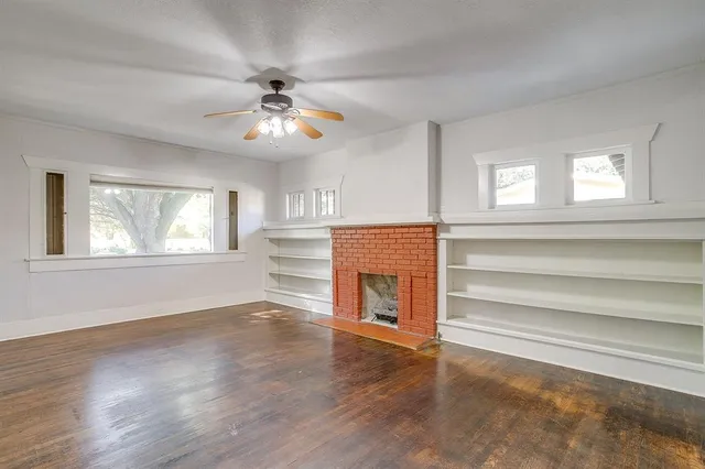 a view of an empty room with wooden floor fireplace and a window