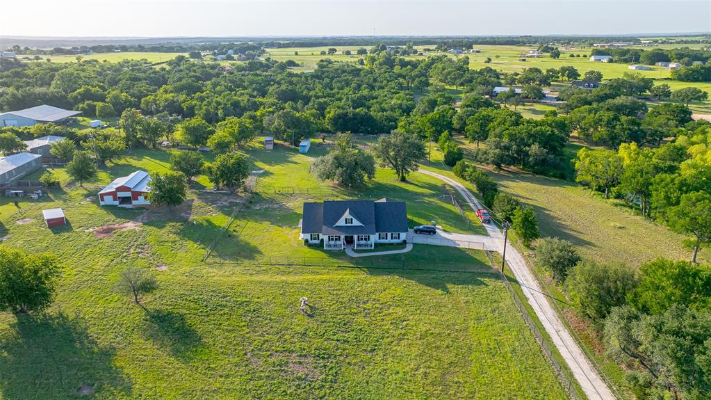 1920 Meander Road Granbury, TX 76049 - Photo 36 of 40 Expansive property featuring a white residence with a dark roof and a covered front porch, surrounded by lush green landscapes and mature trees