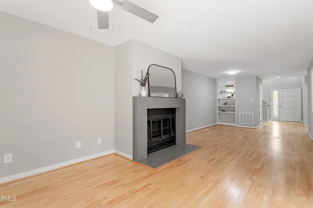 a view of an empty room with wooden floor fireplace and a window