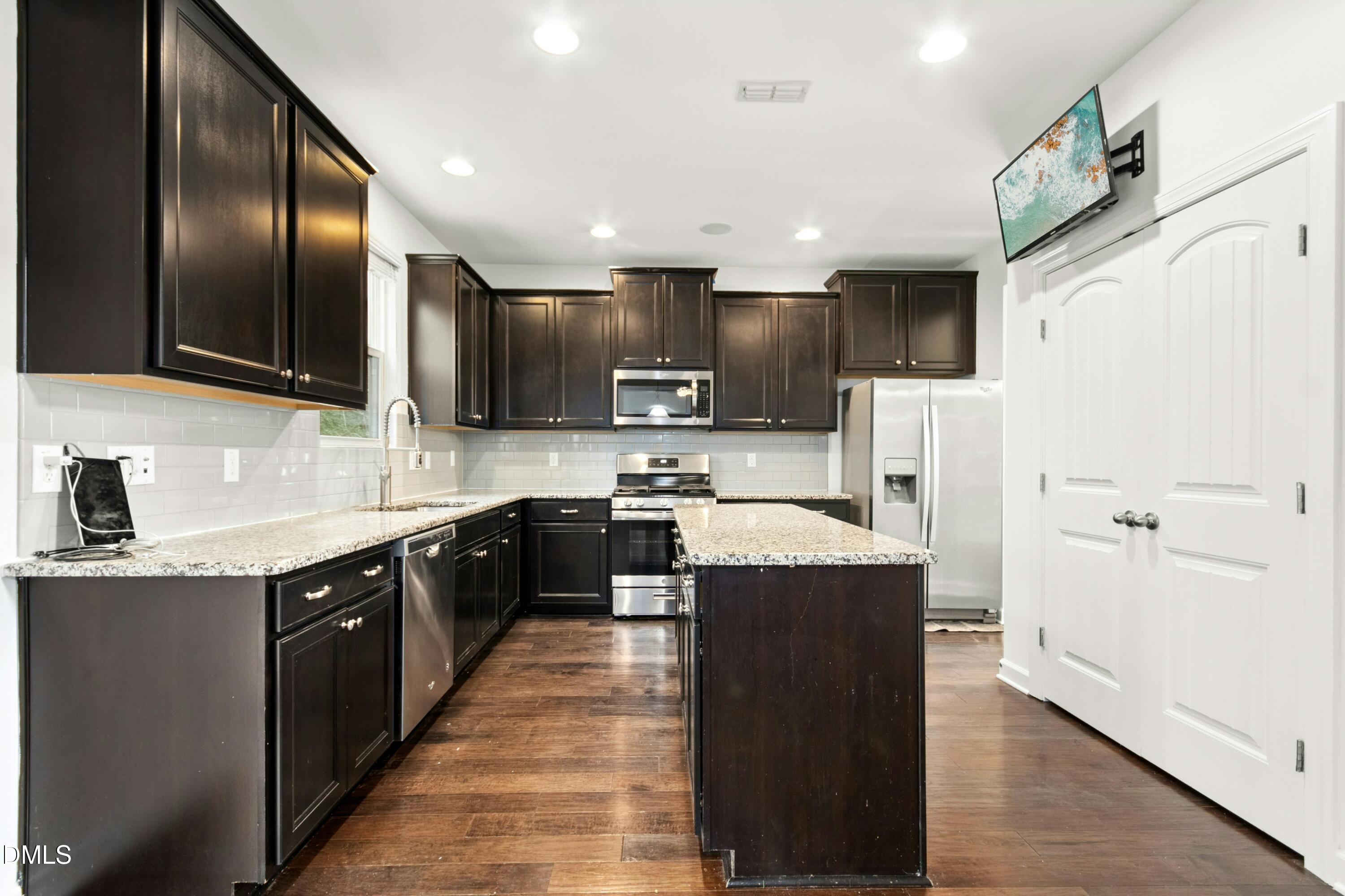 125 Spring Pine Lane Holly Springs, NC 27540 - Photo 8 of 34 a large kitchen with stainless steel appliances kitchen island granite countertop a stove a sink dishwasher and a refrigerator with wooden floor