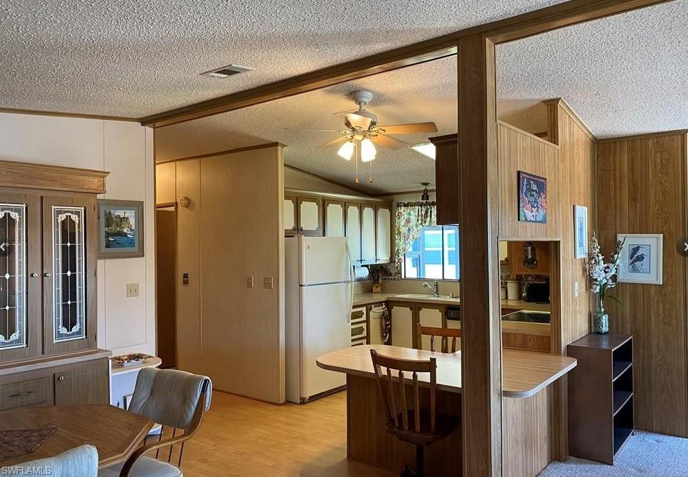 76 Atlantic Way, Unit 76 Naples, FL 34104 - Photo 9 of 18 Kitchen with lofted ceiling, freestanding refrigerator, a breakfast bar area, a textured ceiling, and a peninsula