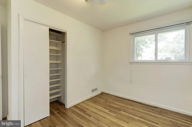 an empty room with wooden floor closet and windows