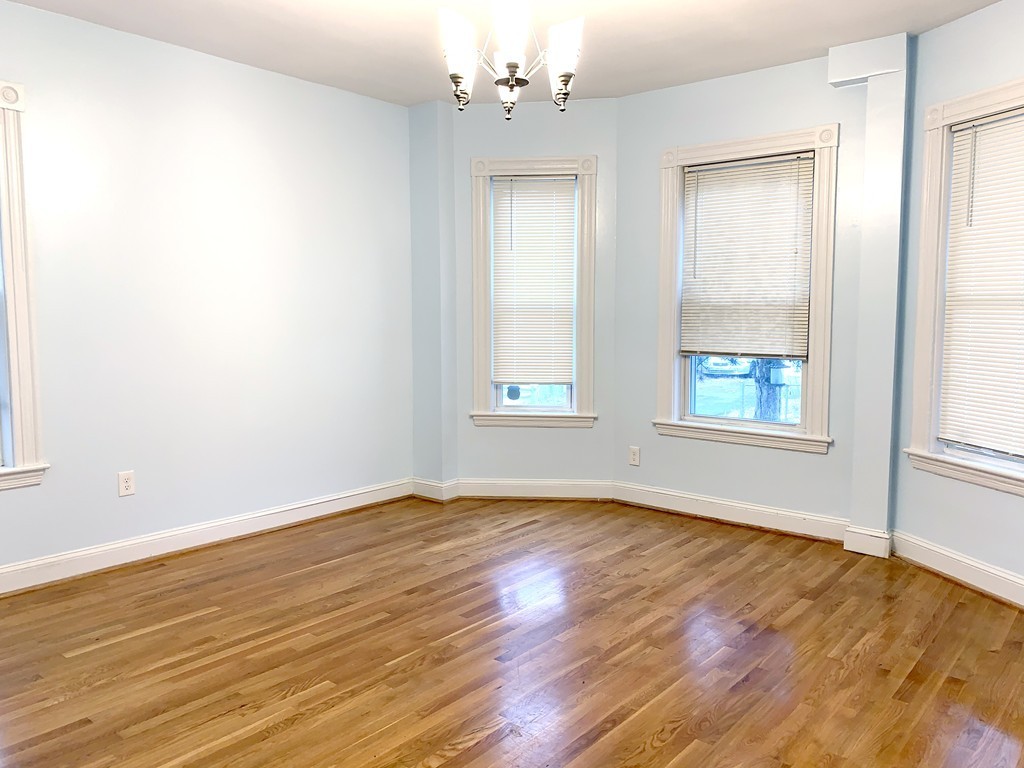 an empty room with wooden floor chandelier fan and windows