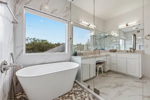 a bathroom with a bathtub a double vanity sink a mirror and a shower