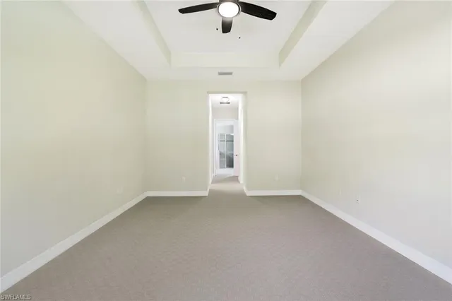 an empty room with chandelier fan and windows