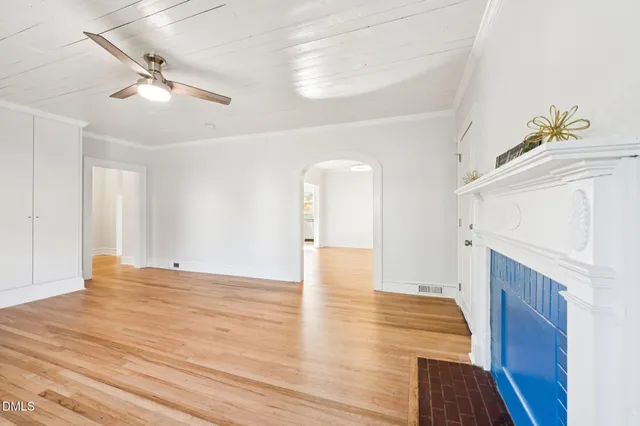 a view of an empty room with chandelier fan and wooden floor