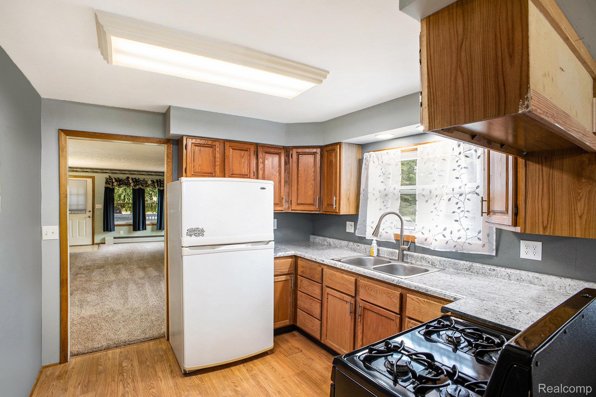 16568 28 Mile Road Albion, MI 49224 - Photo 8 of 26 Kitchen with freestanding refrigerator, light wood finished floors, brown cabinetry, light countertops, and black range with gas stovetop