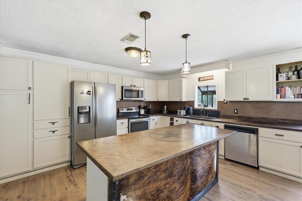 237 Brenda Lane Gainesville, TX 76240 - Photo 11 of 40 Kitchen featuring an expansive center island with a wood-finish countertop, wood-finish flooring, white cabinetry, stainless steel appliances, and a double basin sink