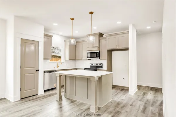 a kitchen with stainless steel appliances kitchen island granite countertop a refrigerator a oven a sink and white cabinets with wooden floor