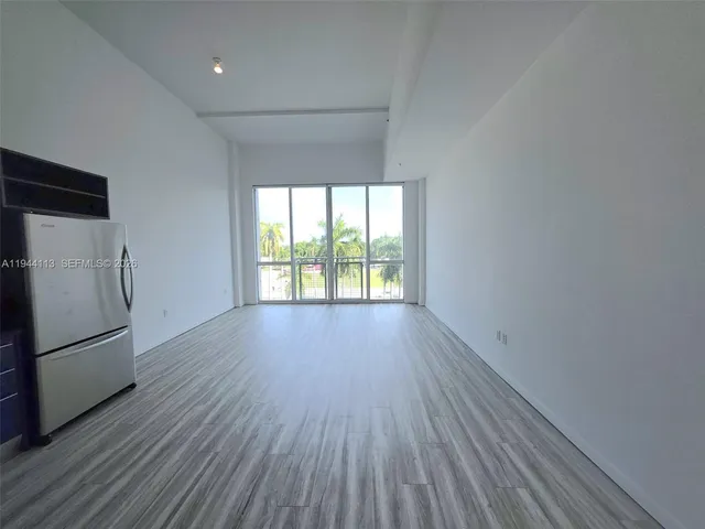 an empty room with wooden floor and a refrigerator