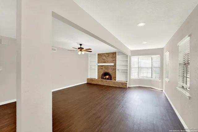 an empty room with wooden floor fireplace and windows