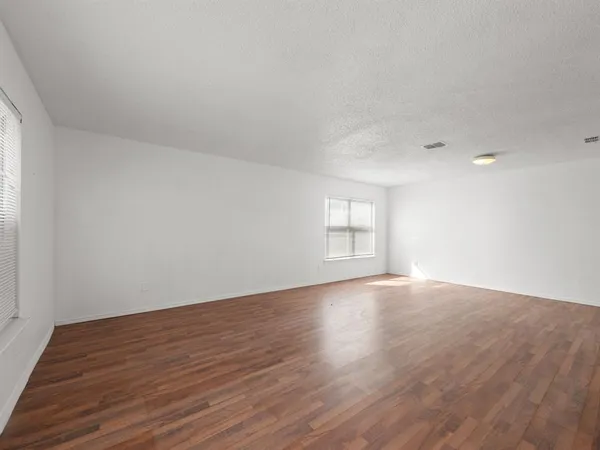a view of an empty room with wooden floor and window