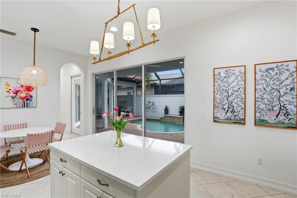 7840 Valencia Court Naples, FL 34113 - Photo 7 of 24 Kitchen featuring white cabinetry, light tile patterned flooring, decorative light fixtures, a center island, and light stone counters