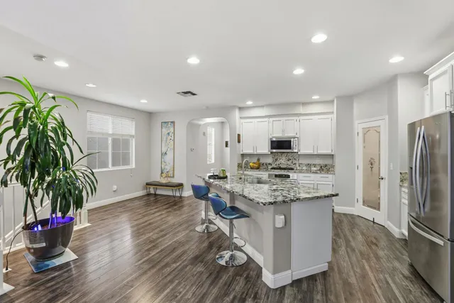 a kitchen with stainless steel appliances kitchen island granite countertop a stove a refrigerator and a dining table with wooden floor