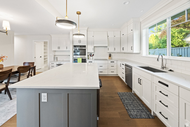 1774 Country Club Drive Logan, UT 84321 - Photo 5 of 28 Modern kitchen featuring a large central island with a light-toned countertop, white cabinetry with dark hardware, stainless steel appliances, a subway tile backsplash, and wood-finish flooring