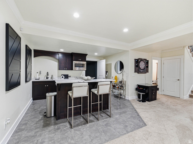 1154 Sunset Dunes Way Draper, UT 84020 - Photo 41 of 50 Kitchen with light countertops, a kitchen breakfast bar, ornamental molding, dark wood finish cabinets, and a center island