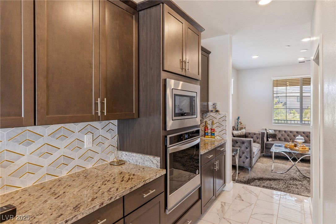 5592 Hickory Tree Street Las Vegas, NV 89149 - Photo 32 of 87 Kitchen with light stone countertops, dark brown cabinets, tasteful backsplash, stainless steel appliances, and light marble finish flooring