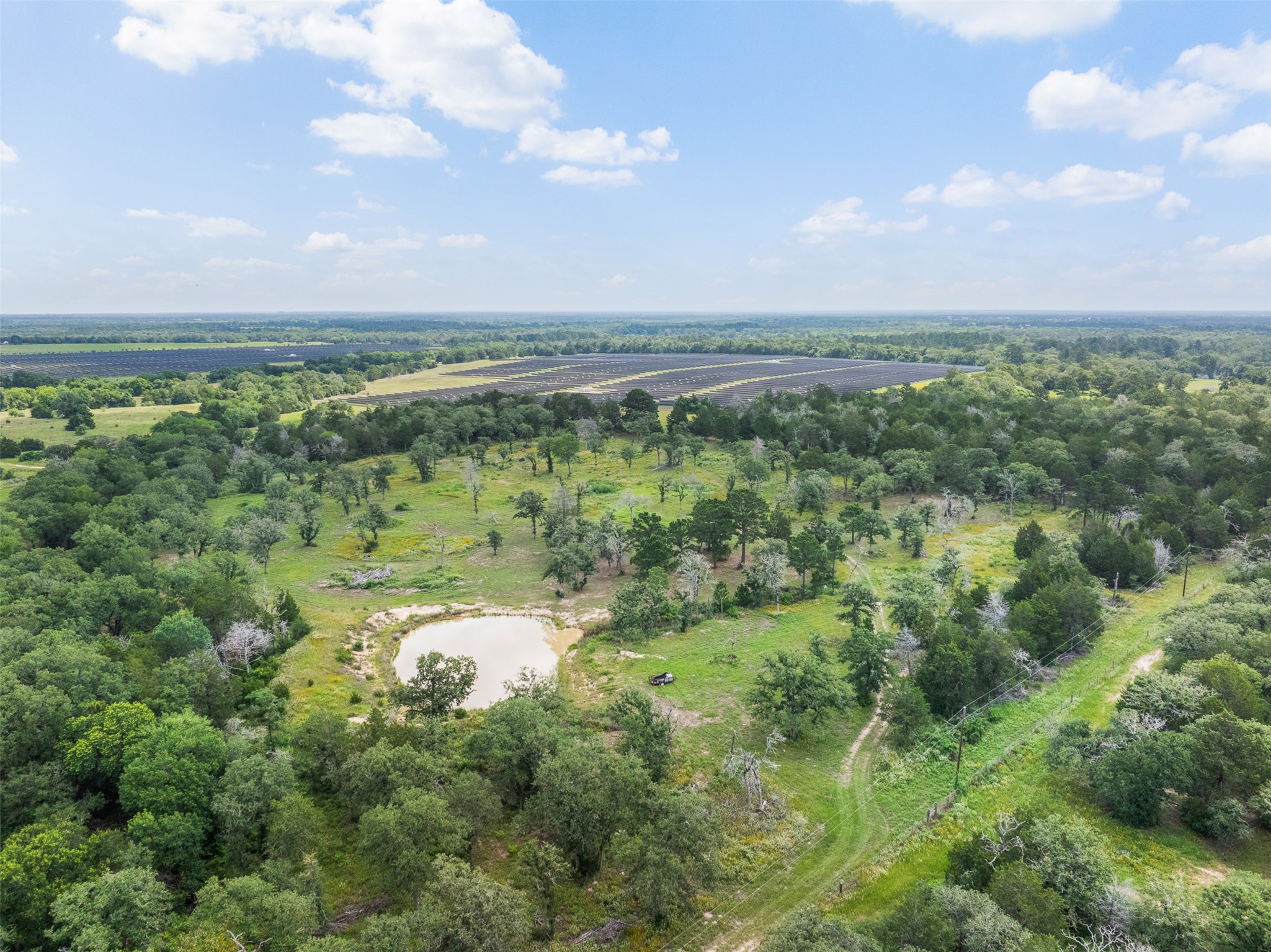 305 Cistern Road Rosanky, TX 78953 - Photo 1 of 13 A tranquil pond nestles amidst a verdant landscape, complemented by distant solar panels.