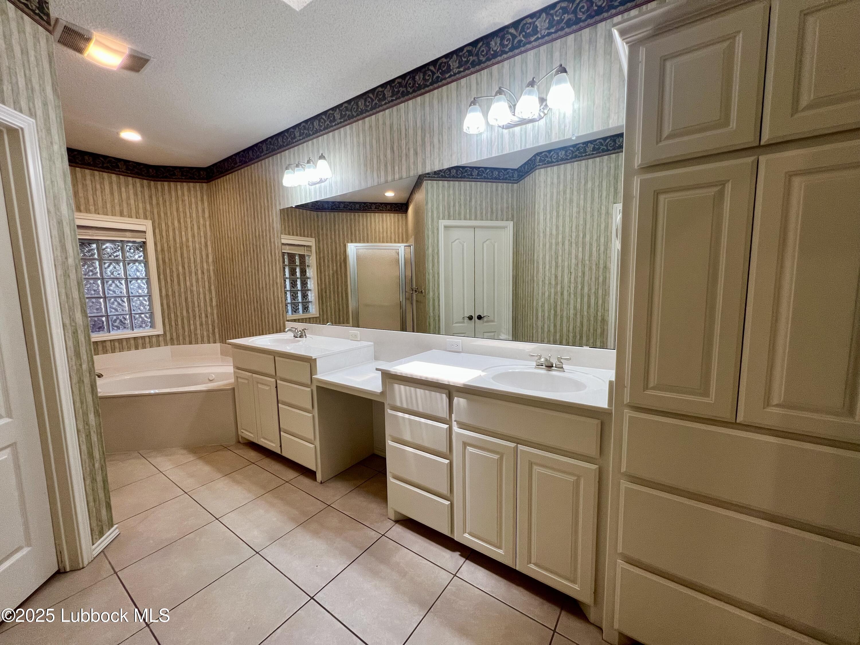 9802 Toledo Avenue Lubbock, TX 79424 - Photo 27 of 64 a bathroom with a double vanity sink a mirror and a bathtub