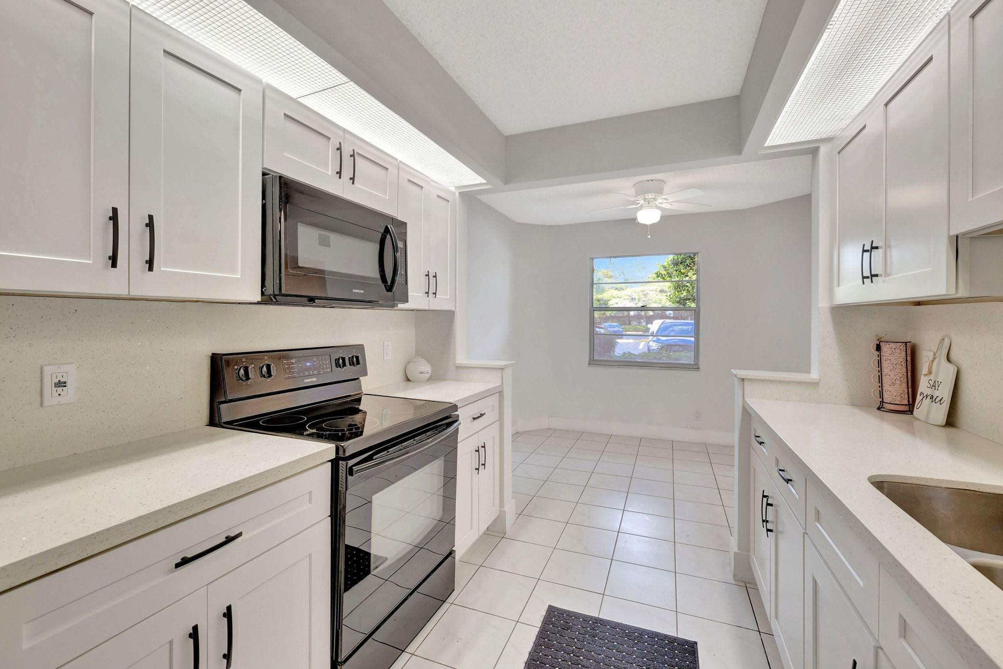 1801 Eleuthera Point, Unit E1 Coconut Creek, FL 33066 - Photo 7 of 50 a kitchen with granite countertop a sink a stove a microwave and cabinets