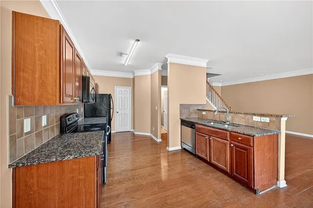 a kitchen with stainless steel appliances granite countertop a stove top oven a sink dishwasher and a refrigerator with wooden cabinets