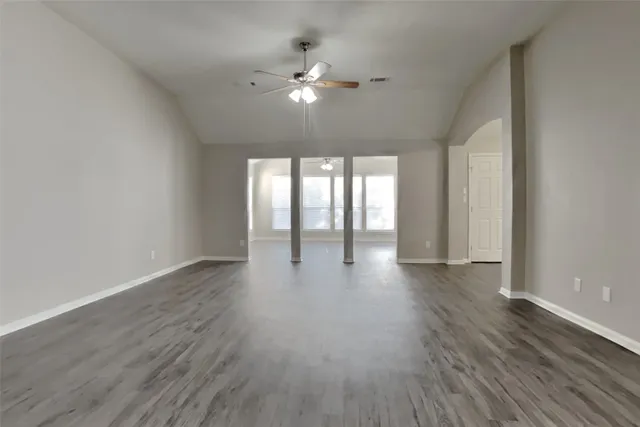 a view of an empty room with wooden floor and fan