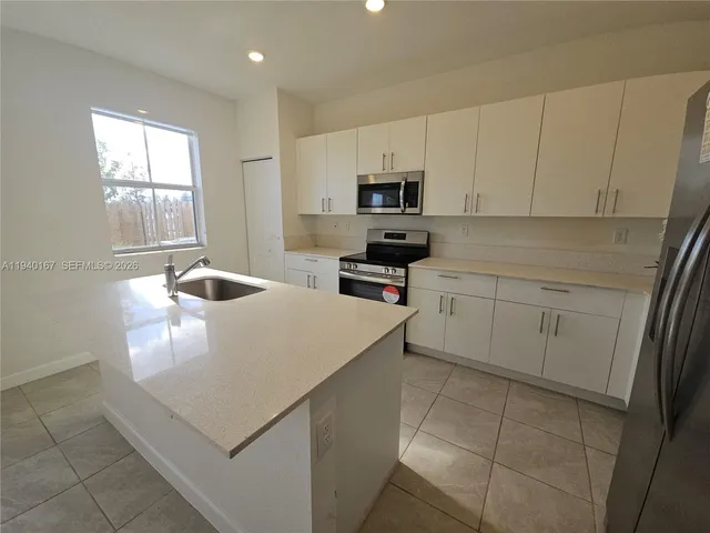 a kitchen with stainless steel appliances a white stove top oven a sink a refrigerator and white cabinets