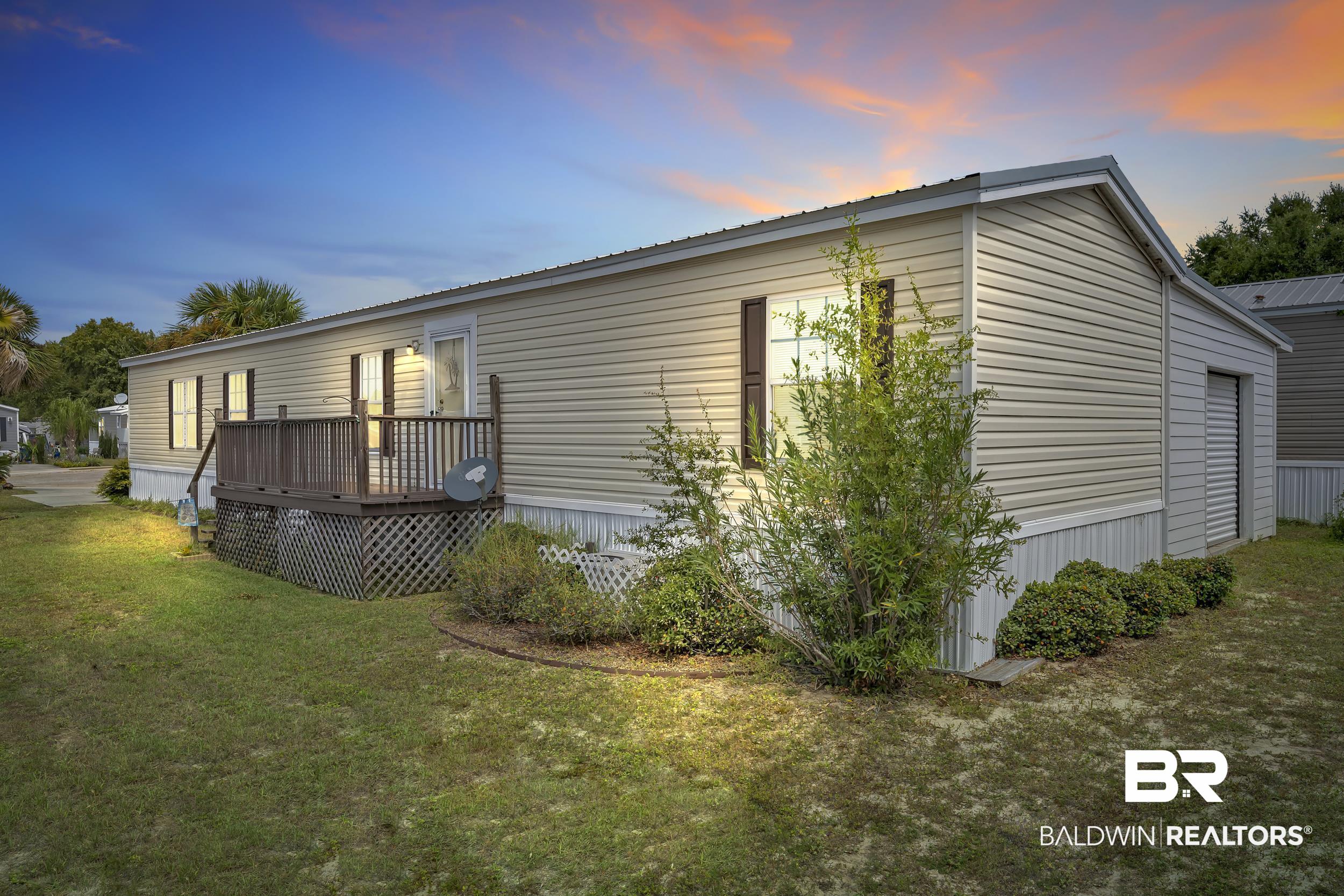 16707 Fort Morgan Road, Unit 8 Gulf Shores, AL 36542 - Photo 1 of 27 Property exterior at dusk with a yard, a wooden deck, and a metal roof